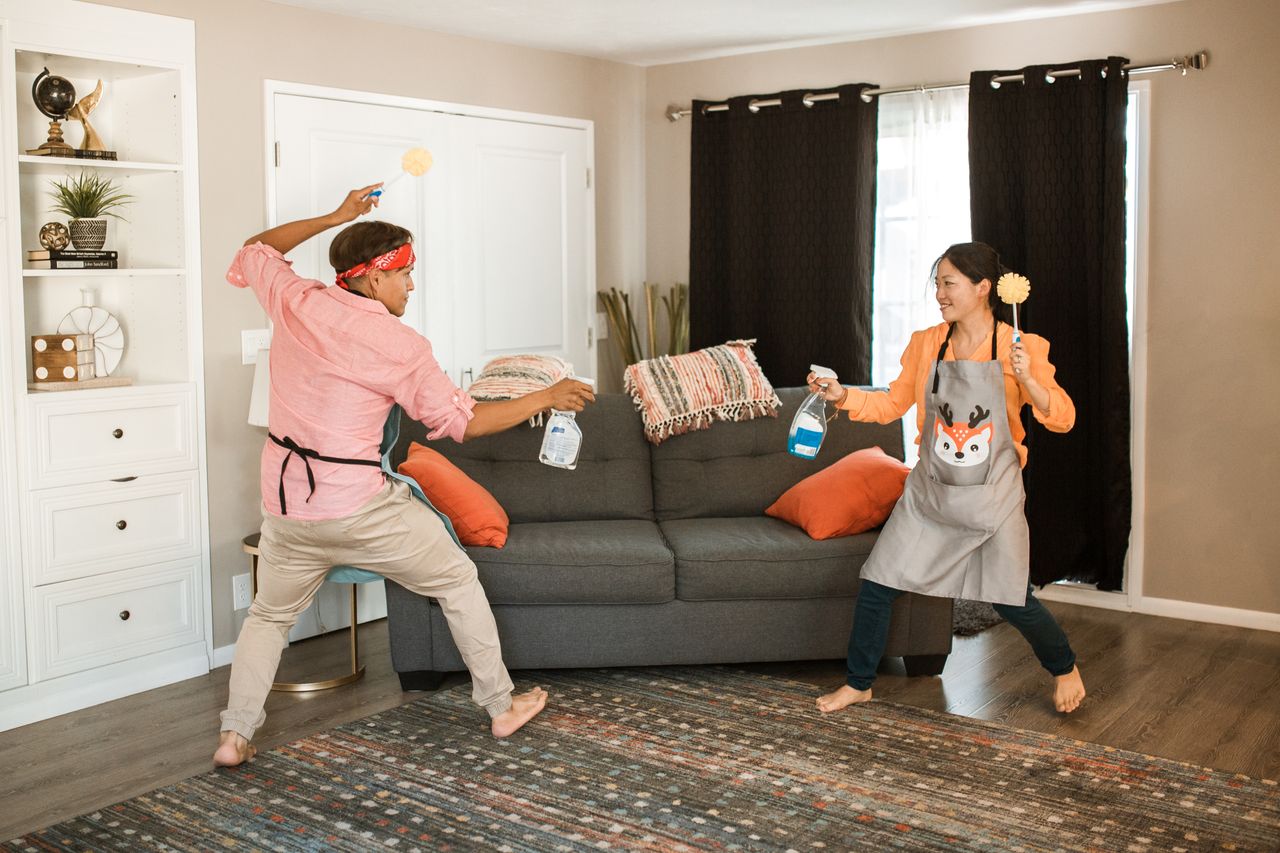 A joyful couple engages in a playful cleaning fight in their living room, showcasing light-hearted domestic life.